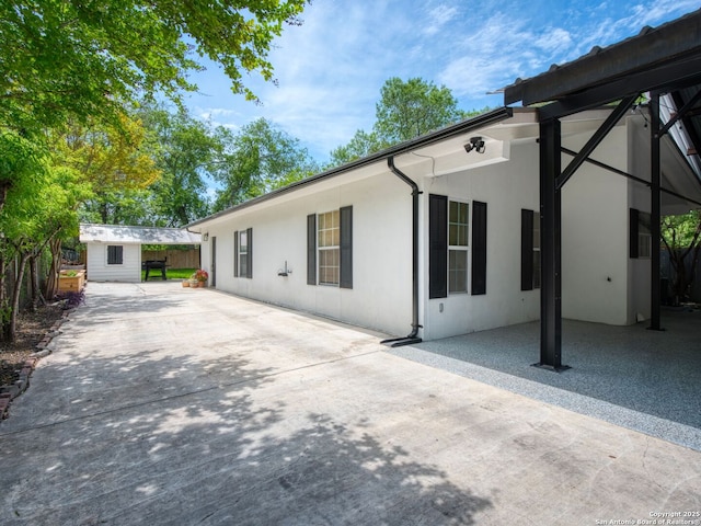 exterior space featuring driveway, a patio, a shed, an outbuilding, and stucco siding