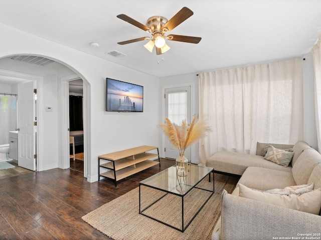 living area featuring dark wood-style flooring, a ceiling fan, visible vents, baseboards, and arched walkways