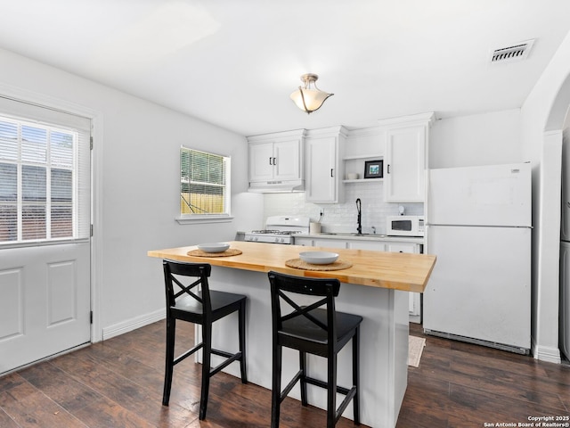 kitchen featuring white appliances, butcher block countertops, under cabinet range hood, a sink, and visible vents