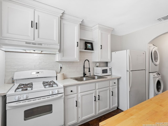 kitchen with a sink, stacked washing maching and dryer, under cabinet range hood, visible vents, and white appliances