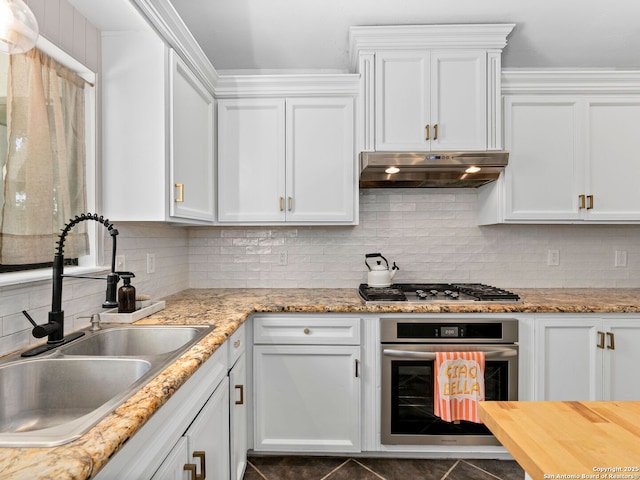 kitchen featuring white cabinetry, a sink, appliances with stainless steel finishes, under cabinet range hood, and backsplash