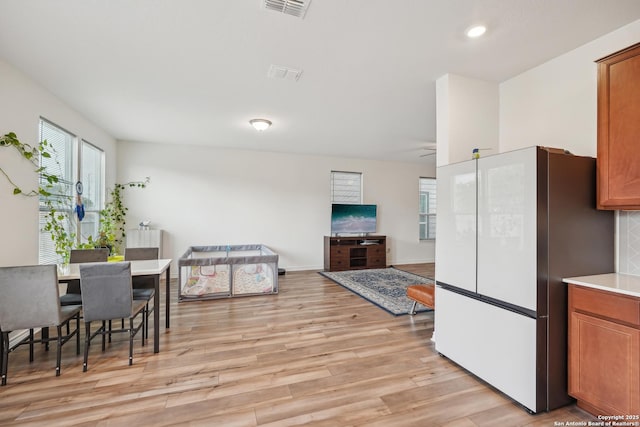 kitchen with brown cabinetry, freestanding refrigerator, light wood-style flooring, and light countertops