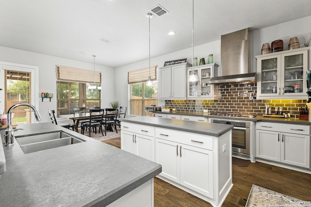 kitchen with wall chimney range hood, a sink, dark countertops, stainless steel appliances, and a kitchen island