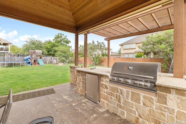 view of patio / terrace featuring a trampoline, a fenced backyard, grilling area, a playground, and exterior kitchen