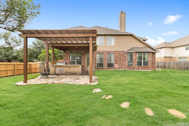 rear view of house with a chimney, a fenced backyard, an outdoor kitchen, a patio area, and a lawn