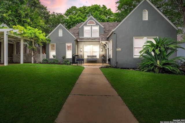 view of front facade featuring a yard, stucco siding, a pergola, and fence
