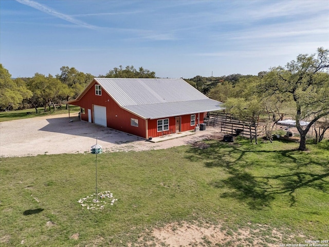 view of property exterior featuring driveway, an outdoor structure, metal roof, a lawn, and a garage