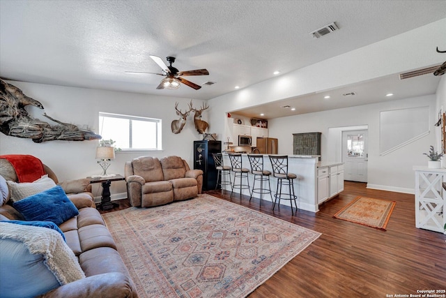 living area featuring ceiling fan, dark wood-style flooring, baseboards, visible vents, and a textured ceiling
