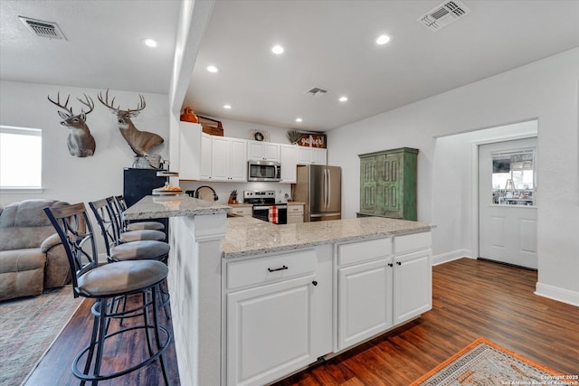 kitchen with appliances with stainless steel finishes, visible vents, a peninsula, and dark wood finished floors