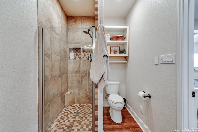 bathroom featuring toilet, a textured wall, tiled shower, and wood finished floors
