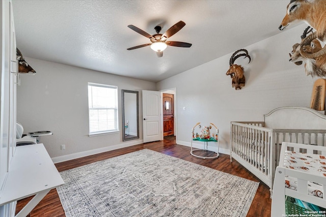 bedroom featuring baseboards, a crib, a ceiling fan, and dark wood-style floors