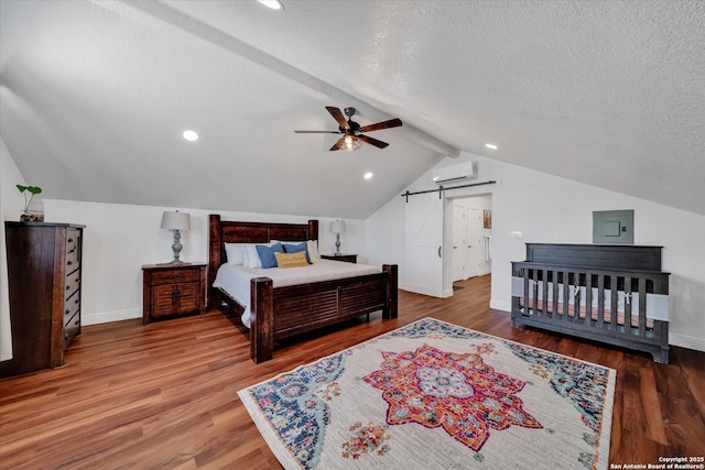 bedroom featuring lofted ceiling, a textured ceiling, baseboards, wood finished floors, and a wall mounted air conditioner