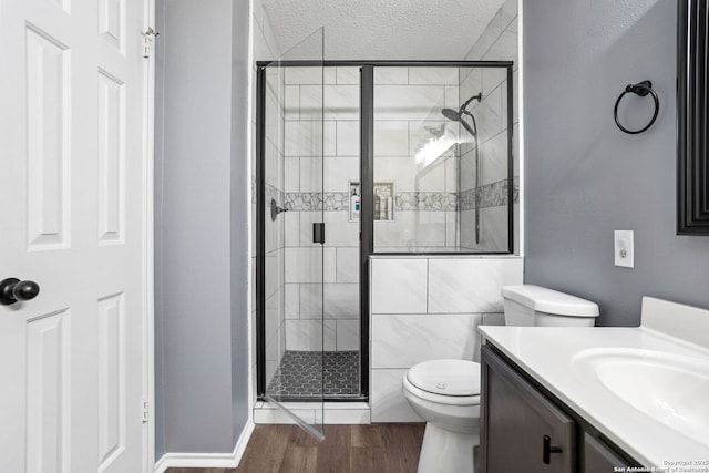full bathroom featuring vanity, toilet, a stall shower, a textured ceiling, and wood finished floors