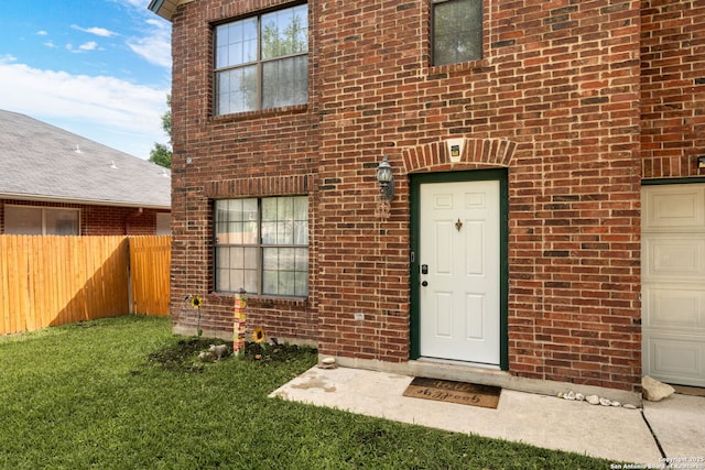 property entrance with brick siding, fence, and a lawn