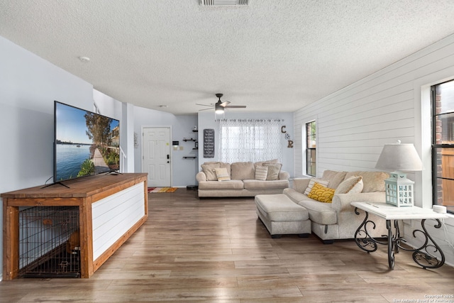 living room featuring a textured ceiling, wood finished floors, a ceiling fan, and visible vents