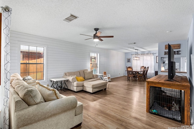 living room featuring visible vents, wood finished floors, ceiling fan, and a textured ceiling