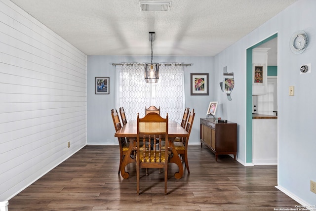 dining room featuring a textured ceiling, visible vents, an inviting chandelier, wooden walls, and dark wood finished floors