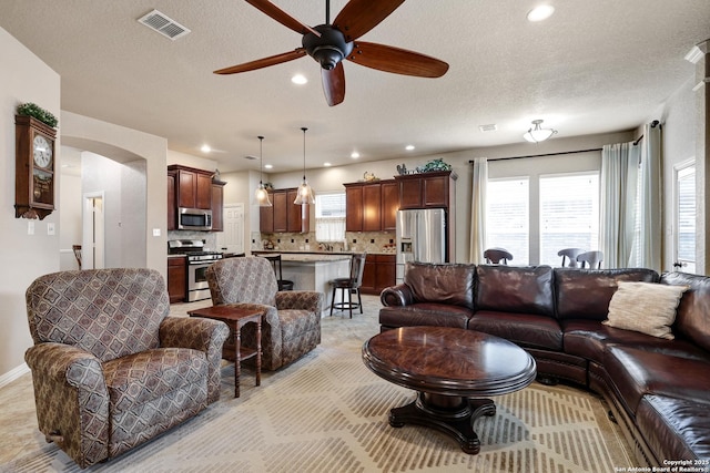 living area featuring visible vents, recessed lighting, a textured ceiling, arched walkways, and a ceiling fan