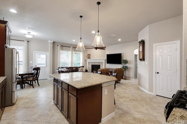 kitchen featuring dark brown cabinets, a tiled fireplace, freestanding refrigerator, open floor plan, and visible vents