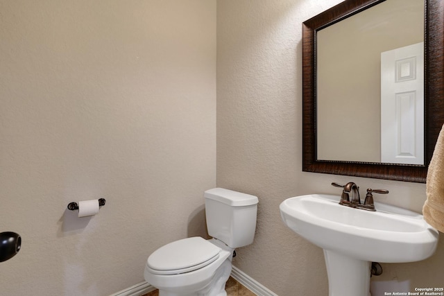 half bath with baseboards, a sink, a textured wall, and toilet