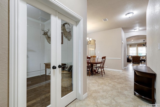 hall with french doors, a textured ceiling, arched walkways, baseboards, and light tile patterned flooring