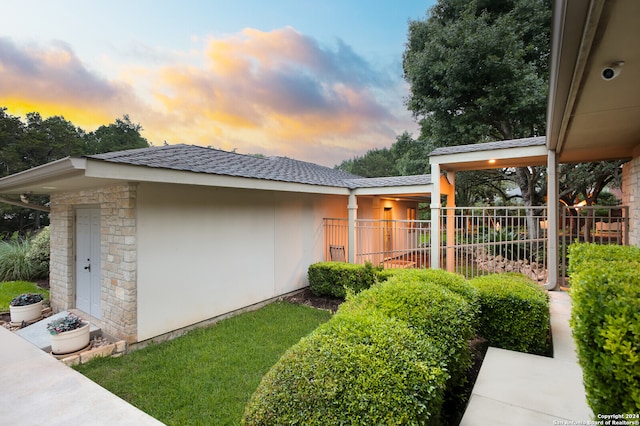 property exterior at dusk with fence, a shingled roof, stucco siding, and stone siding