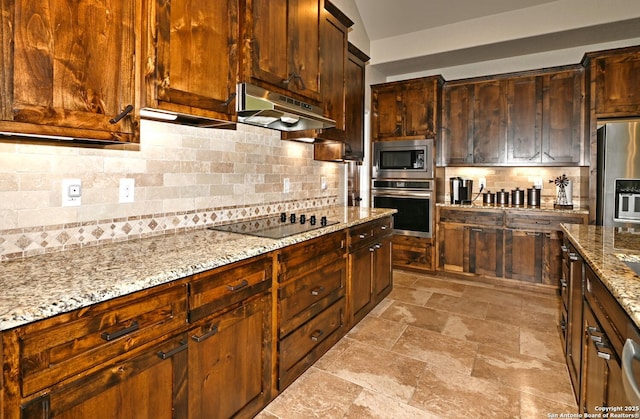 kitchen featuring light stone countertops, stone finish floor, stainless steel appliances, backsplash, and under cabinet range hood