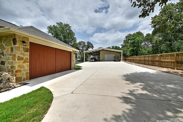 view of side of home featuring roof with shingles, fence, stone siding, and a garage