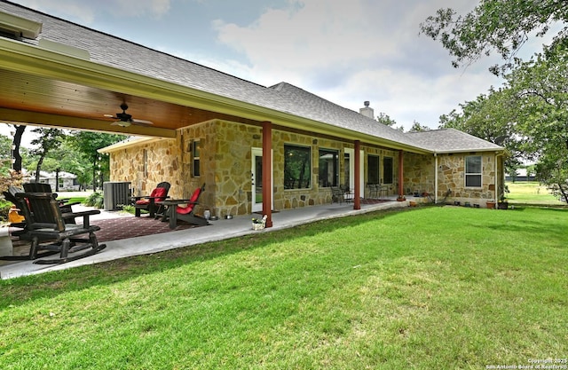 back of property with stone siding, a chimney, a ceiling fan, a patio area, and a yard