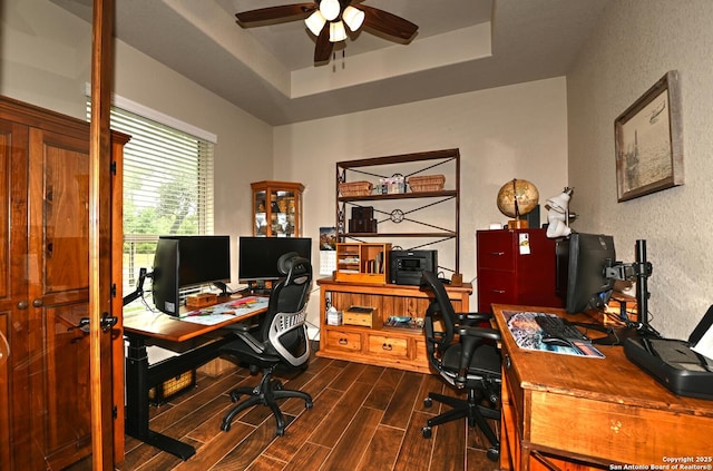 office area featuring a tray ceiling, a textured wall, a ceiling fan, and dark wood-style flooring