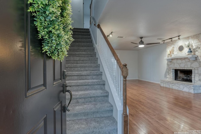 2215 Shady Rock Cir, San Antonio, TX 78231 - stairway featuring a ceiling fan, rail lighting, wood finished floors, and a stone fireplace