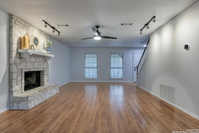 2215 Shady Rock Cir, San Antonio, TX 78231 - unfurnished living room with track lighting, ceiling fan, a stone fireplace, and wood finished floors