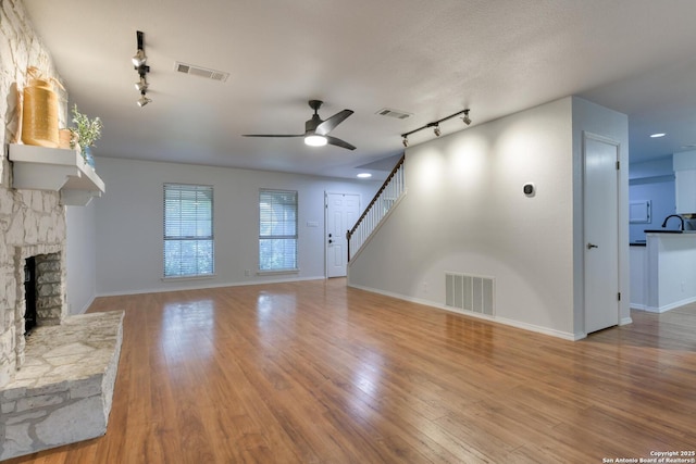 2215 Shady Rock Cir, San Antonio, TX 78231 - unfurnished living room featuring rail lighting, a ceiling fan, a fireplace, wood finished floors, and baseboards
