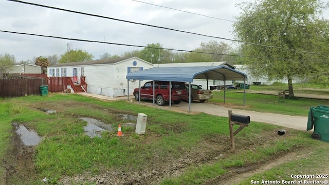 view of parking featuring fence, a carport, and dirt driveway