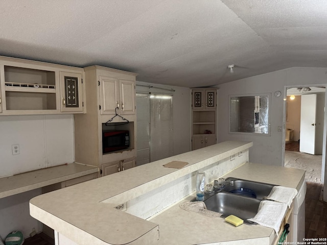 kitchen with black microwave, light countertops, a sink, and lofted ceiling