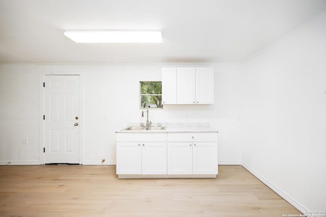 kitchen with light wood-style floors, baseboards, light countertops, white cabinetry, and a sink