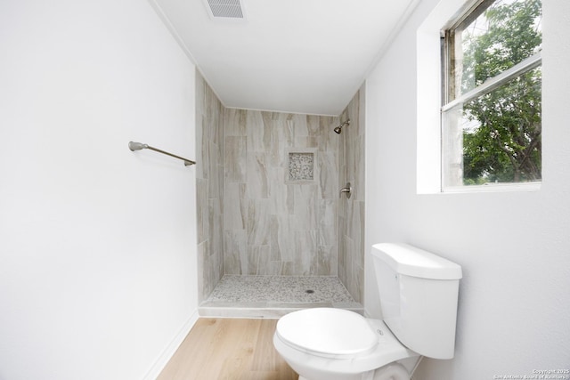 bathroom with visible vents, a tile shower, toilet, and a wealth of natural light