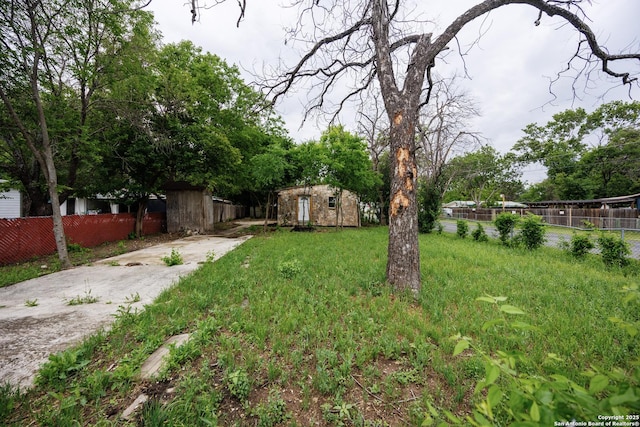 view of yard featuring concrete driveway, fence, an outdoor structure, and a shed