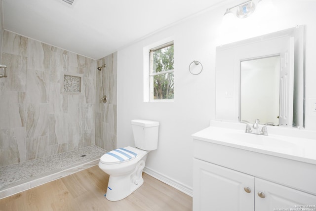 bathroom with a tile shower, vanity, toilet, baseboards, and wood finished floors
