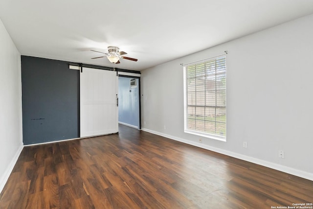 empty room featuring baseboards, a barn door, and wood finished floors