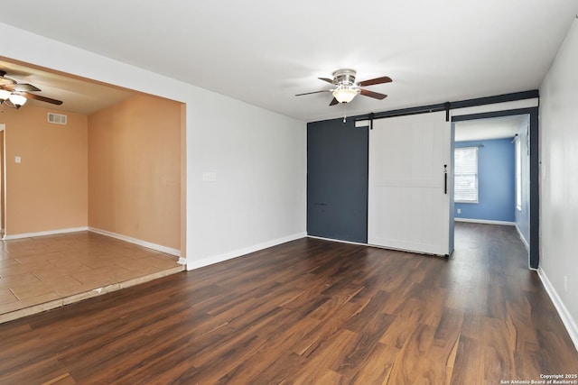 empty room with ceiling fan, a barn door, baseboards, visible vents, and dark wood-style floors
