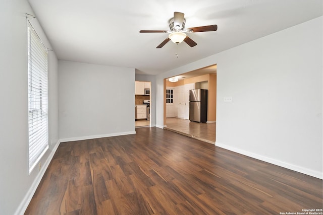 unfurnished living room featuring baseboards, ceiling fan, dark wood-type flooring, and a wealth of natural light