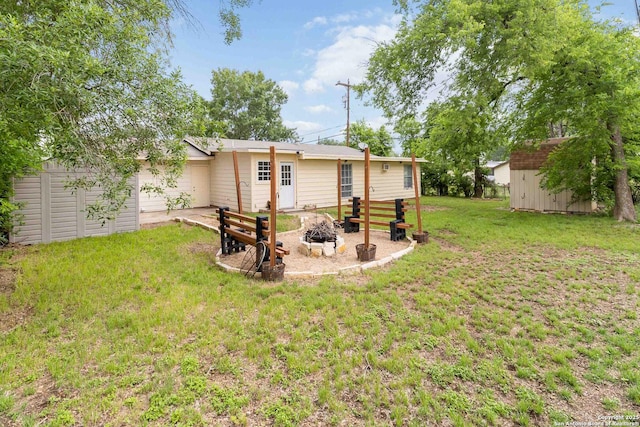 back of property featuring a lawn, an outdoor structure, an outdoor fire pit, and a shed