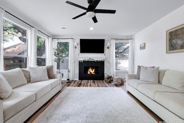 living room featuring a tiled fireplace, ceiling fan, wood finished floors, and visible vents