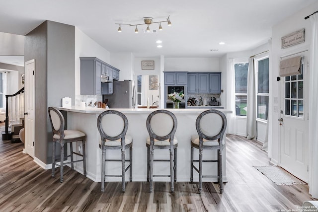 kitchen featuring freestanding refrigerator, a peninsula, a kitchen bar, light wood-style flooring, and blue cabinetry