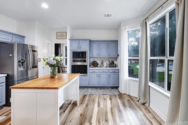kitchen with visible vents, butcher block counters, a kitchen island, light wood-style flooring, and stainless steel appliances