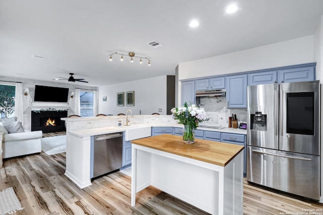 kitchen featuring visible vents, stainless steel appliances, a sink, a peninsula, and under cabinet range hood