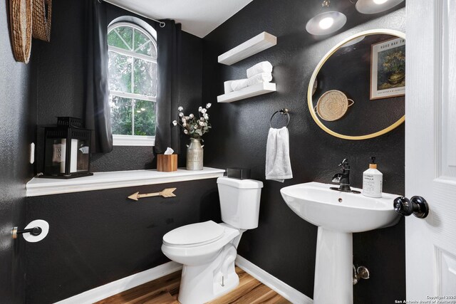 bathroom featuring baseboards, toilet, a textured wall, and wood finished floors