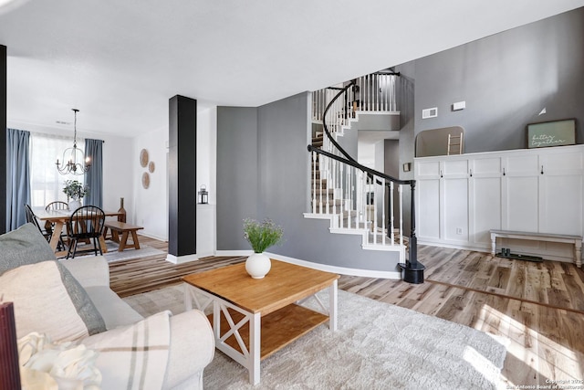 living room with baseboards, light wood finished floors, a chandelier, and stairway