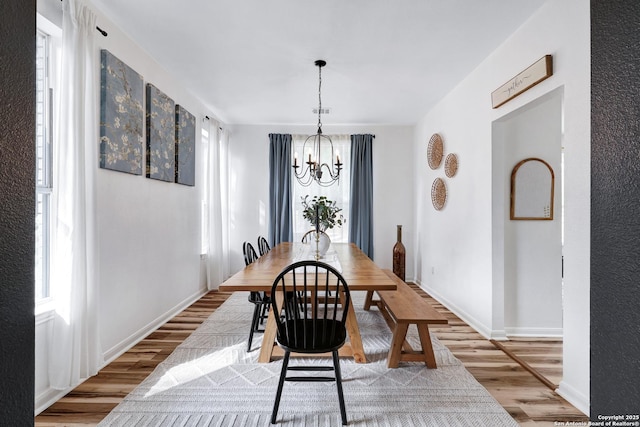 dining space with baseboards, wood finished floors, and a notable chandelier